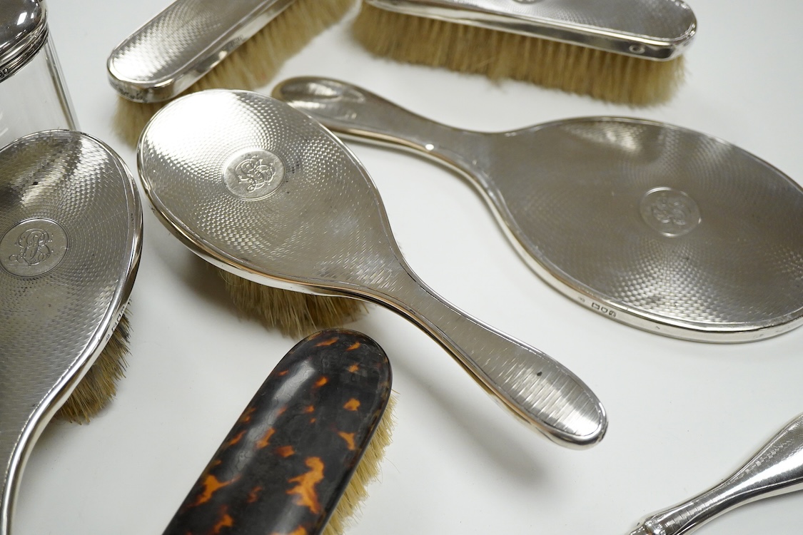 A George V seven piece silver mounted toilet set by Charles Henry Dumenil, comprising a hand mirror, four brushes, a glass toilet jar and button hook, London, 1911/12 & 18, together with one other silver mounted toilet j